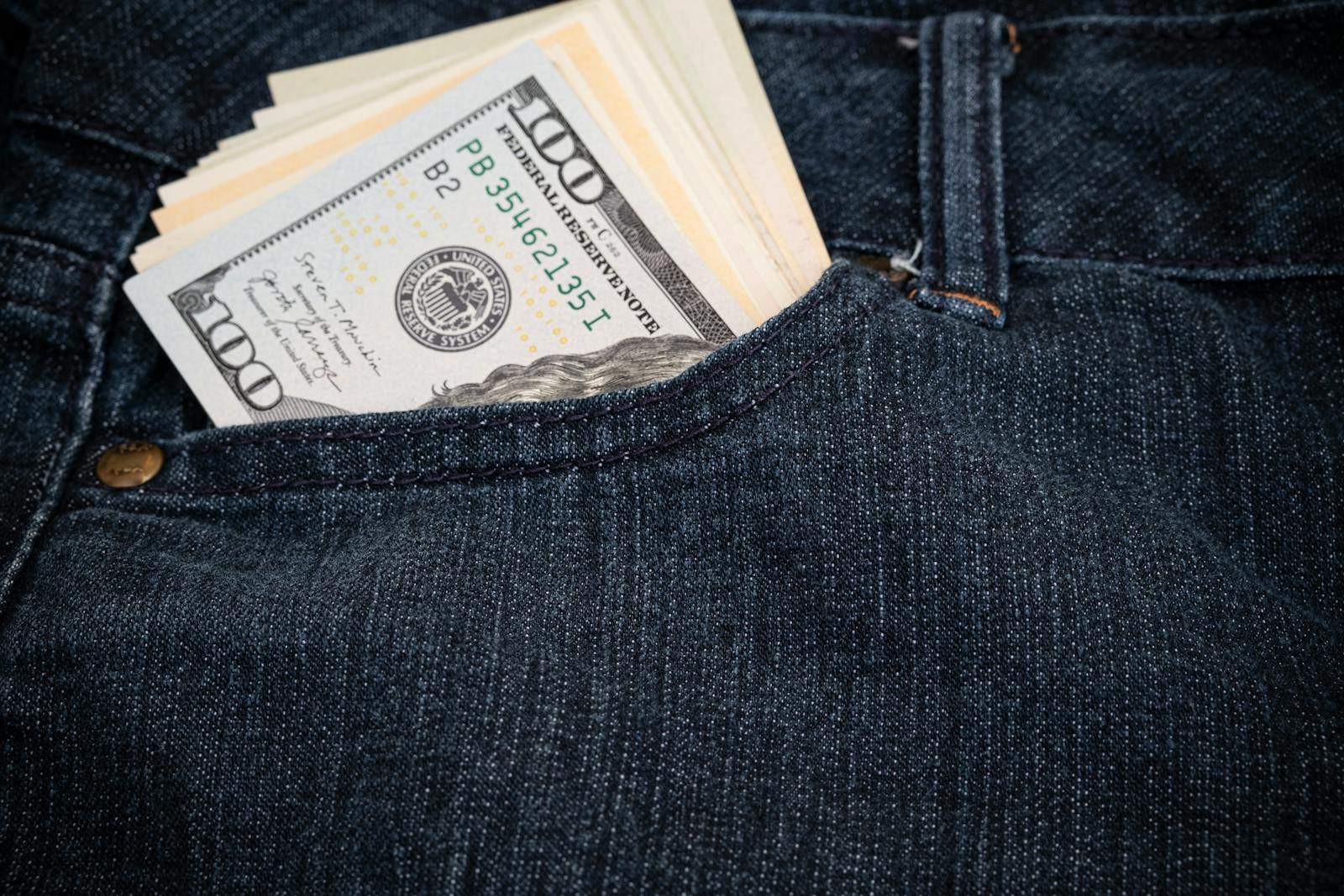 Close-up of hundred-dollar bills in a denim jeans pocket, symbolizing wealth and fashion.